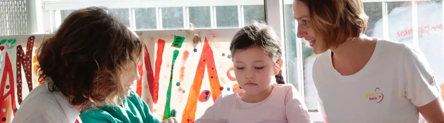 en.Zwei Kinder die neben einer Frau mit mit Fingerfarben malen
