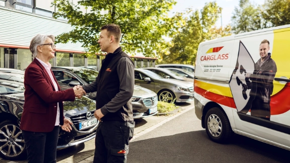 Ein Mitarbeiter von Carglass gibt einer Kundin die Hand. 
