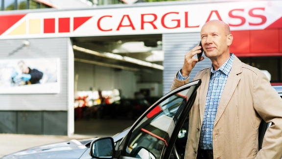 Ein Kunde telefoniert mit seinem Handy vor einem Carglass Service Center.